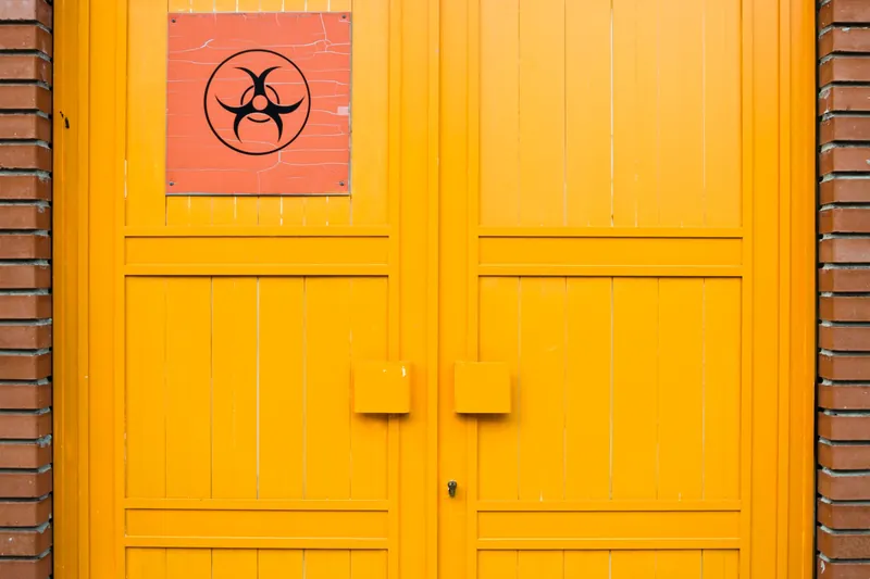 Orange double door with a biohazard warning sign on a red brick wall