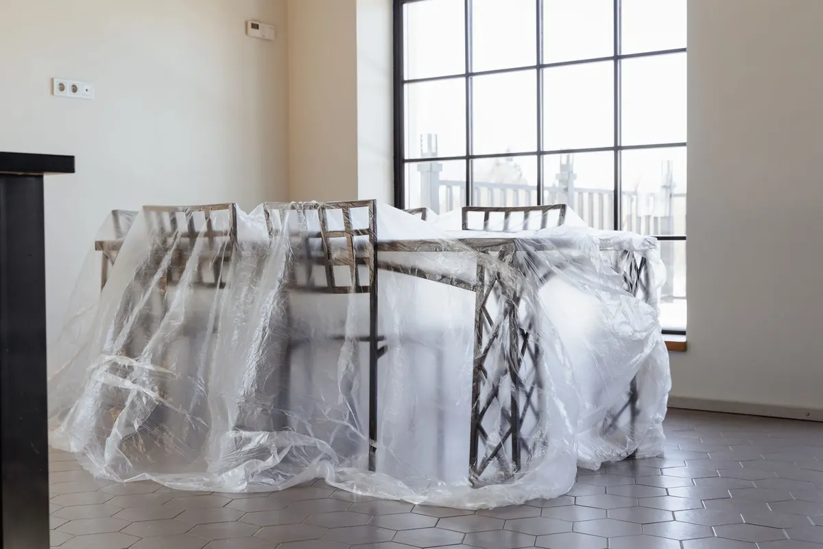 Table and chairs covered in clear plastic sheeting in a bright empty room