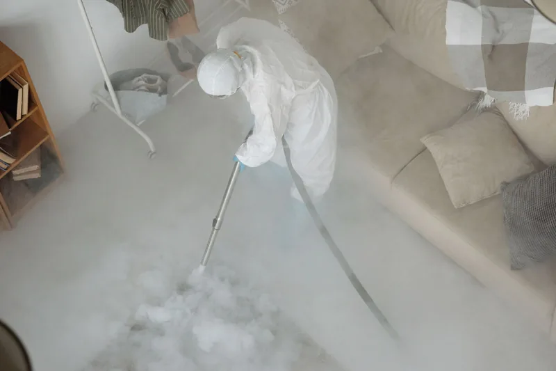 Technician in a white protective suit fogging a room with disinfectant mist, seen from above
